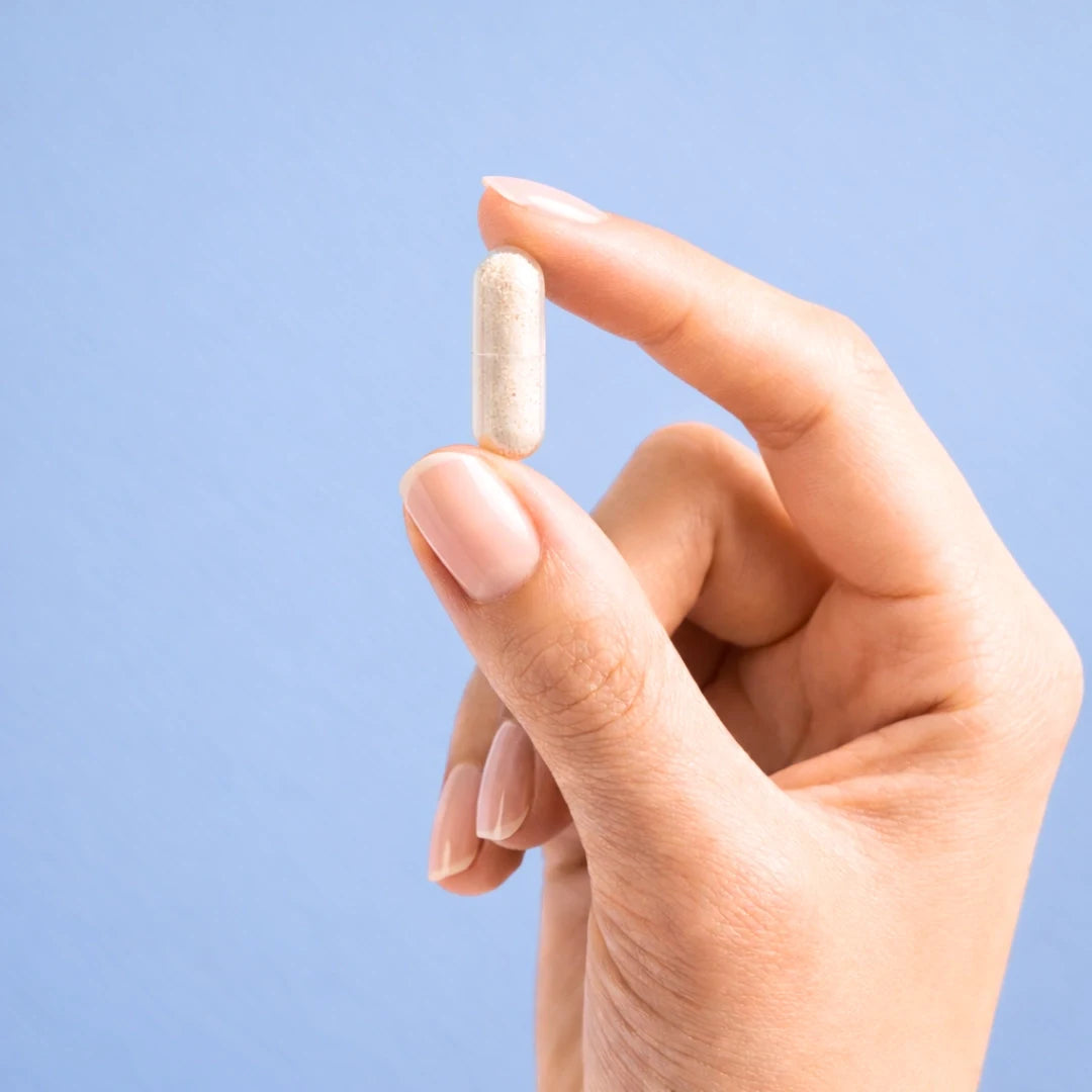 Hand holding a white capsule of Calm by ARYA Lab against a light blue background