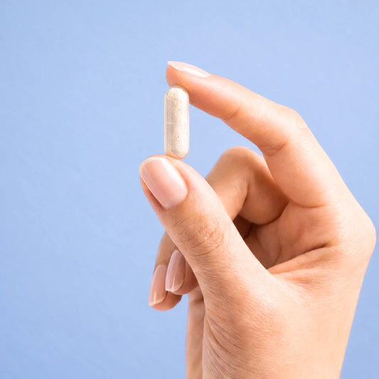 Hand holding a white capsule of Calm by ARYA Lab against a light blue background
