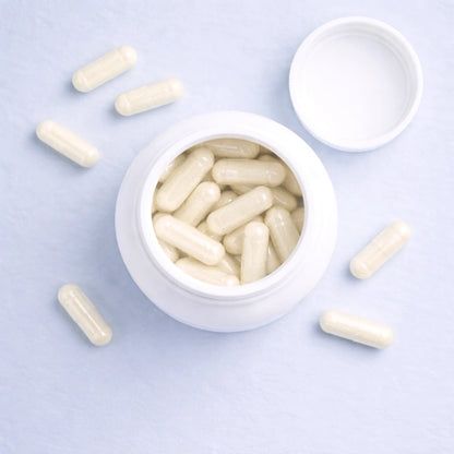 White capsules of Calm by ARYA Lab in an open white container on a light purple background
