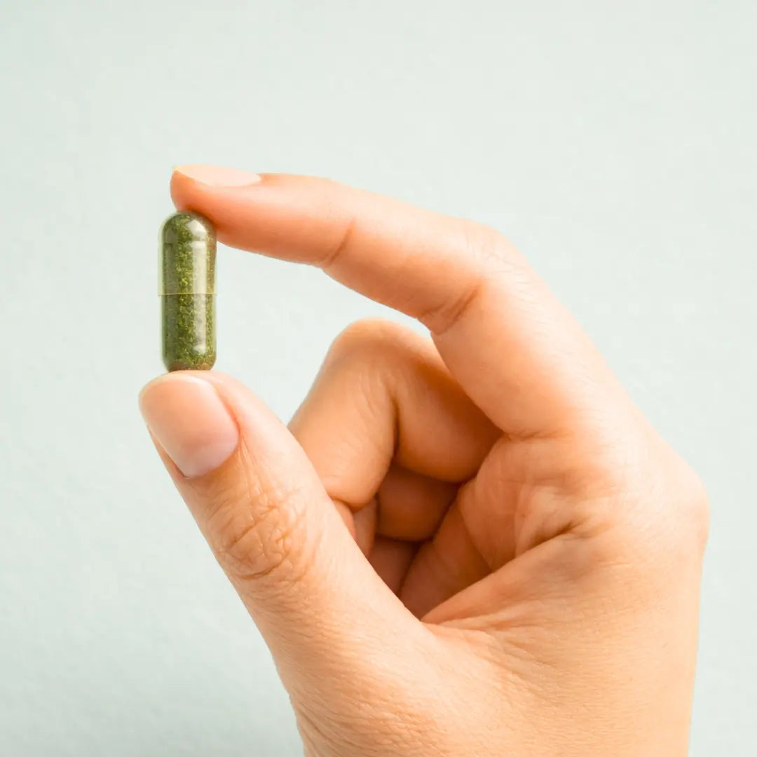 Hand holding a green capsule of Glow by ARYA LAB against a light gray background